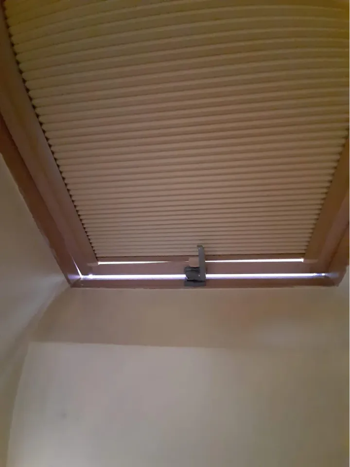 Plisa na oknie dachowym w skosie poddasza, tkanina dociśnięta prowadnicami do szyby